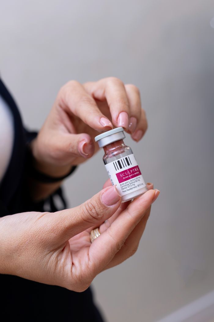 Close-up image of hands holding a Sculptra vial, commonly used in cosmetic procedures.